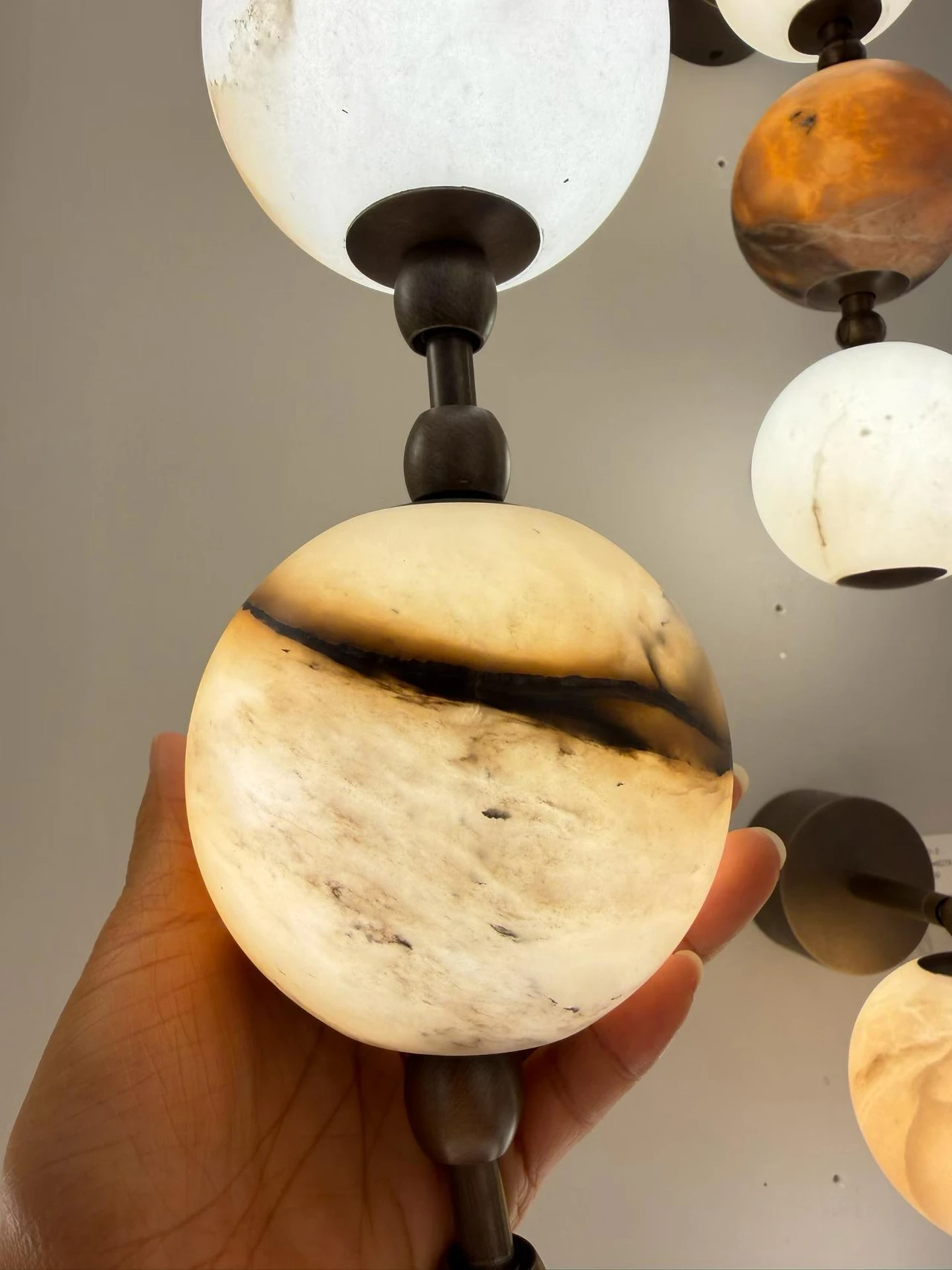 Illuminated veined alabaster globes connected by dark metal fittings