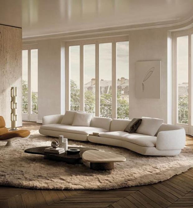 Low-profile curved white sectional sofa beside tall windows
