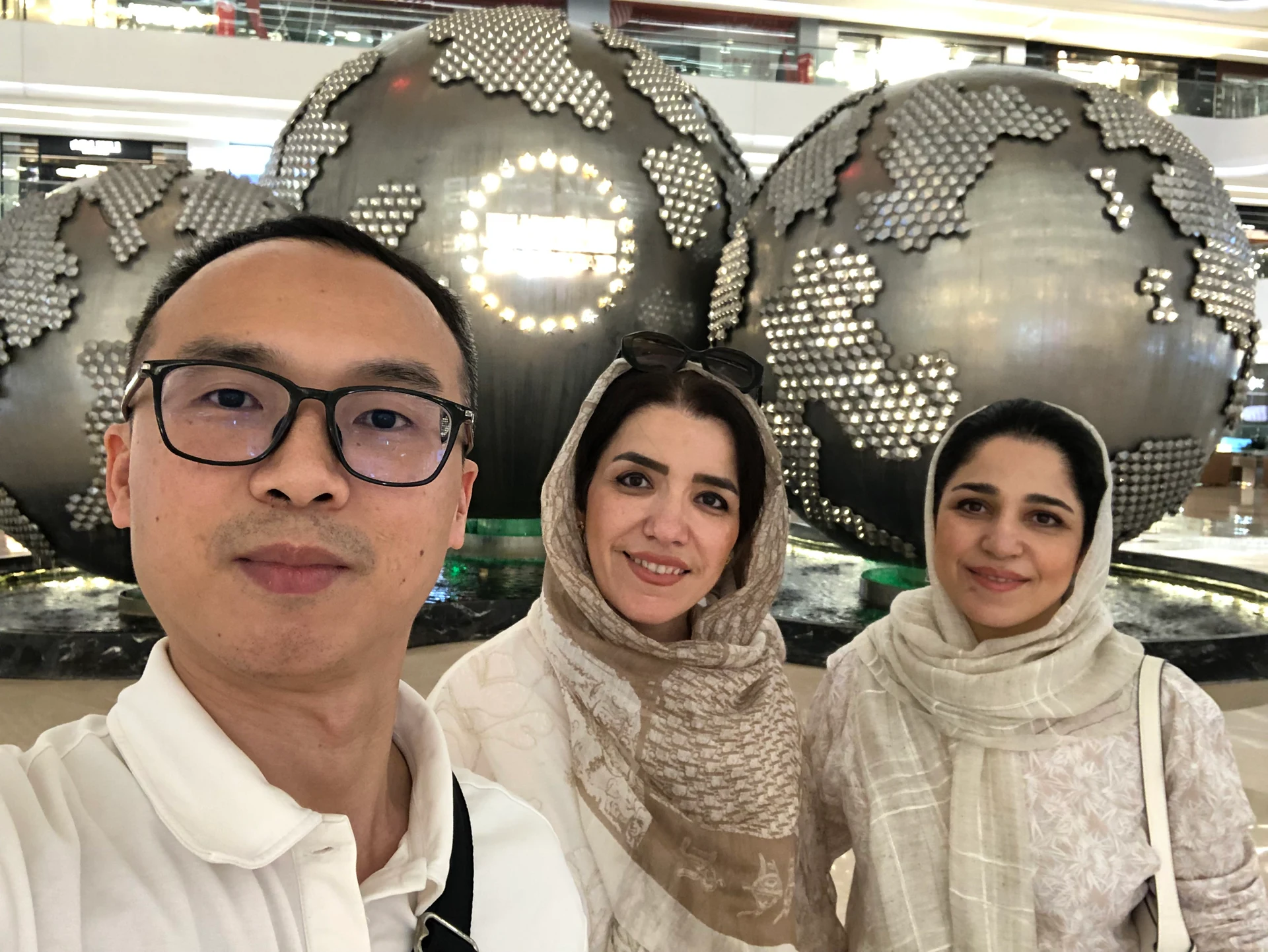 Three people posing in front of large decorative globe sculptures indoors